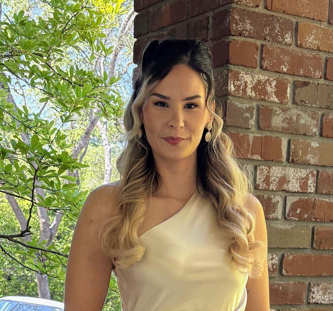 A person posing outdoors next to a brick wall