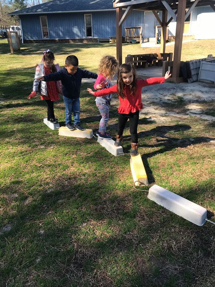 Four children balancing on a low beam in a grassy area