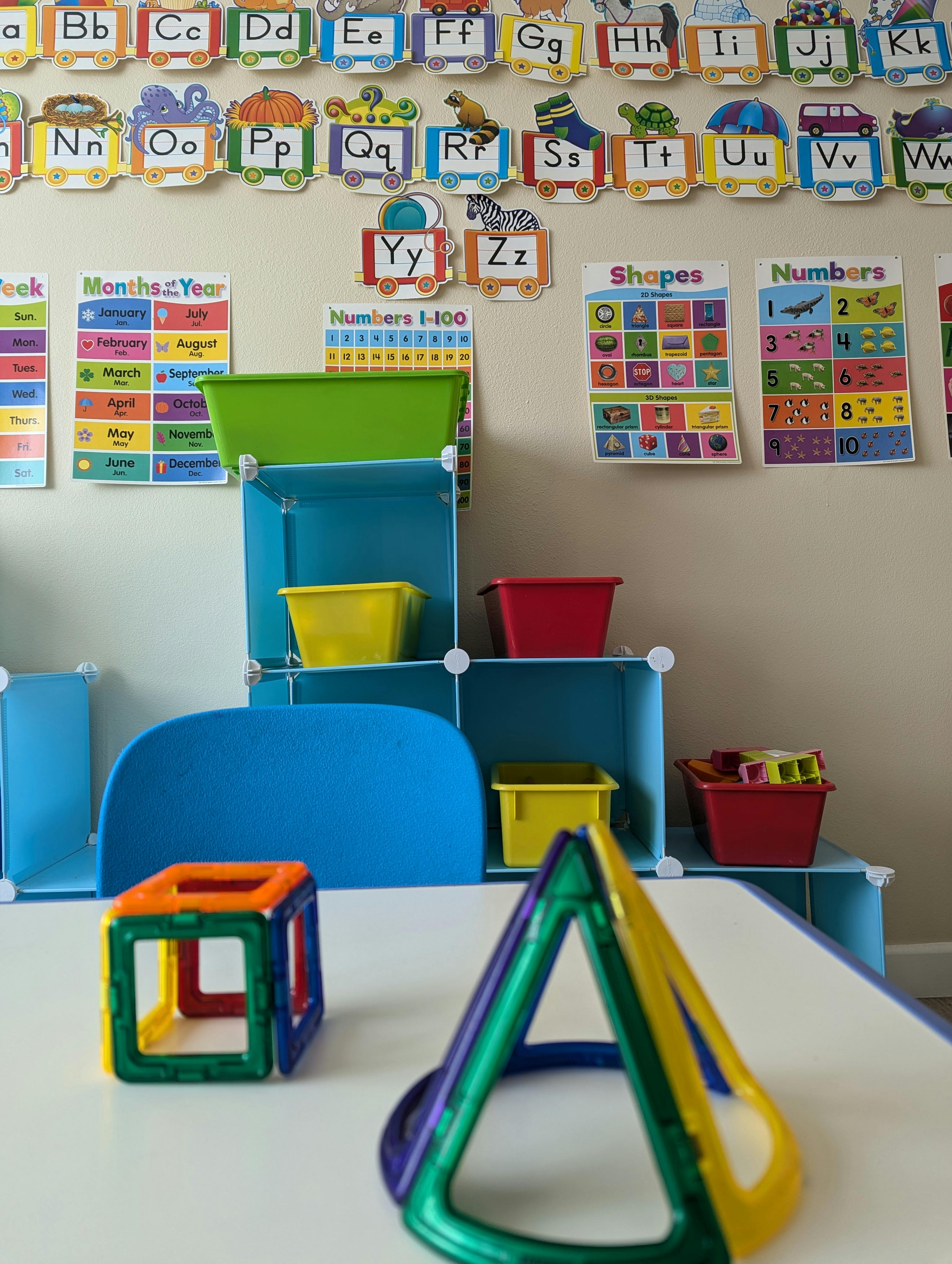 Magnetic shapes on a table in a classroom with alphabet and number charts