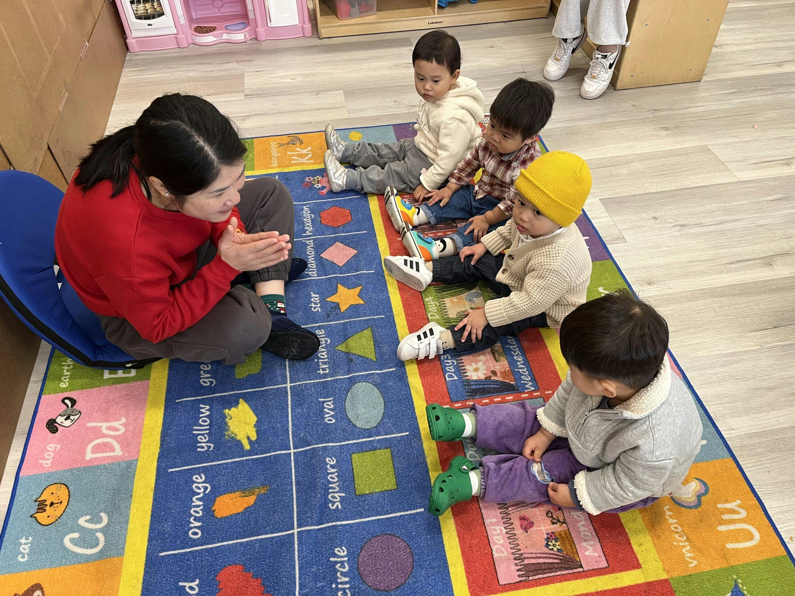 Person and multiple children sitting on a colorful rug in a classroom