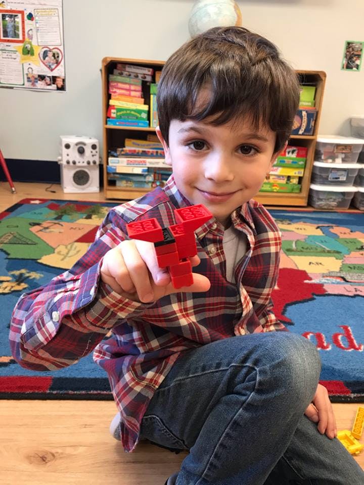 Child in a classroom holding up a red toy