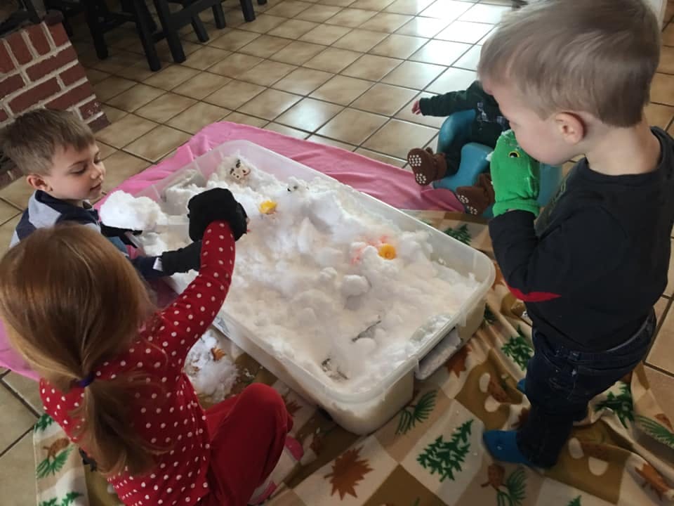 Three children playing with a sensory bin filled with white material