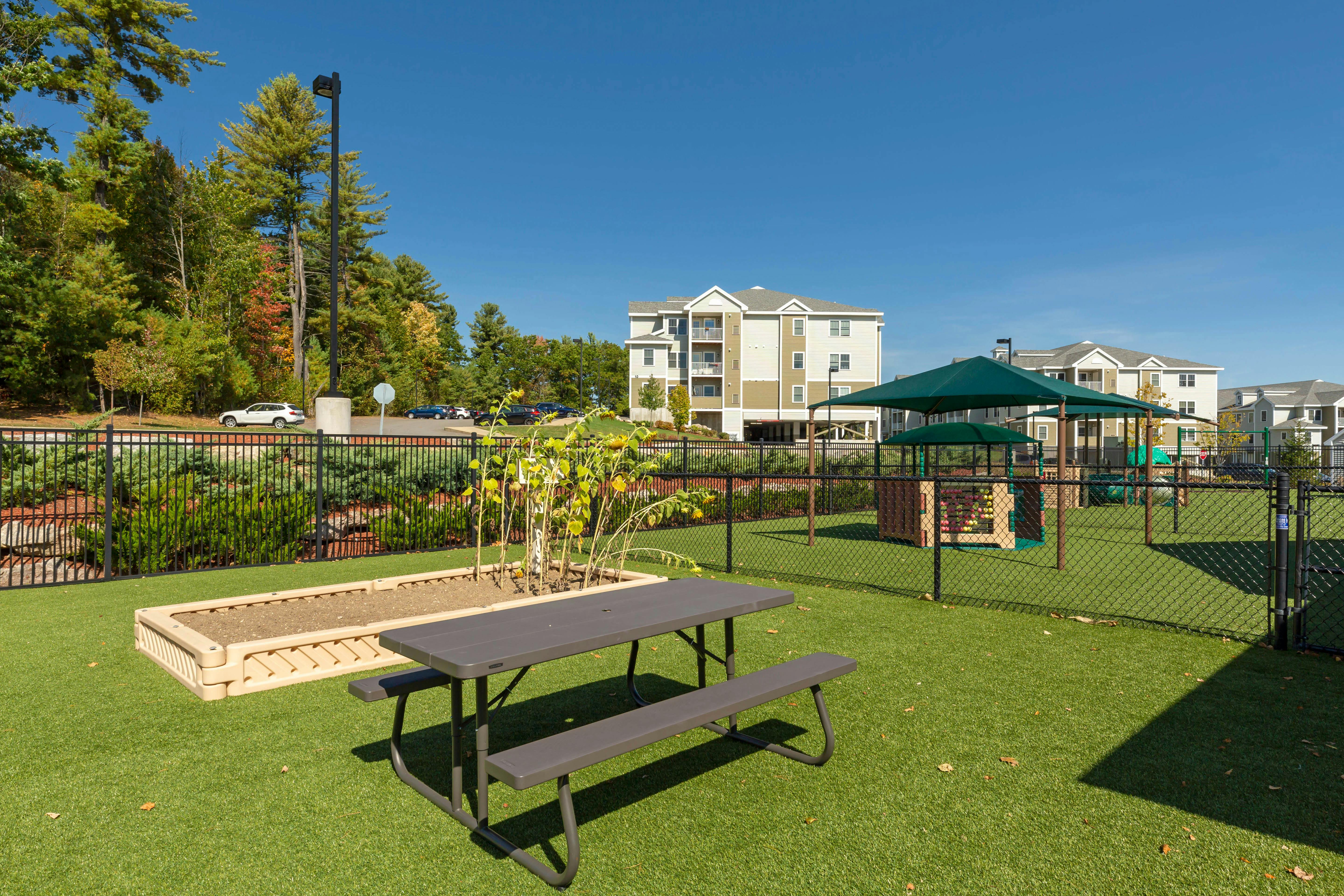 Picnic table and raised garden bed on artificial turf, fenced playground