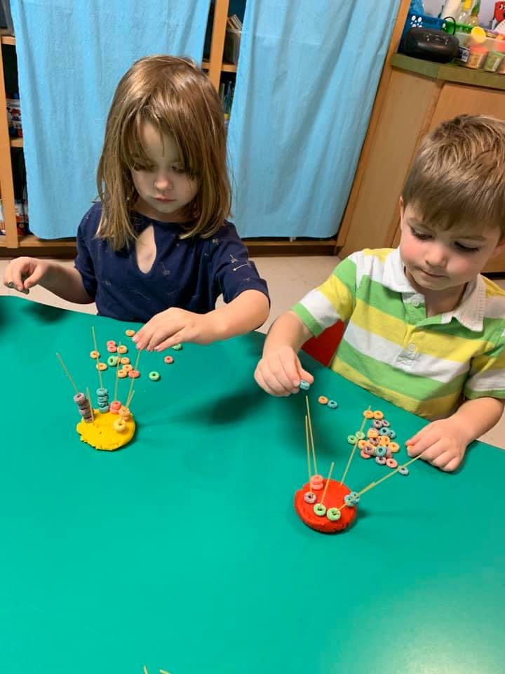 Two children playing with cereal and spaghetti on a green table