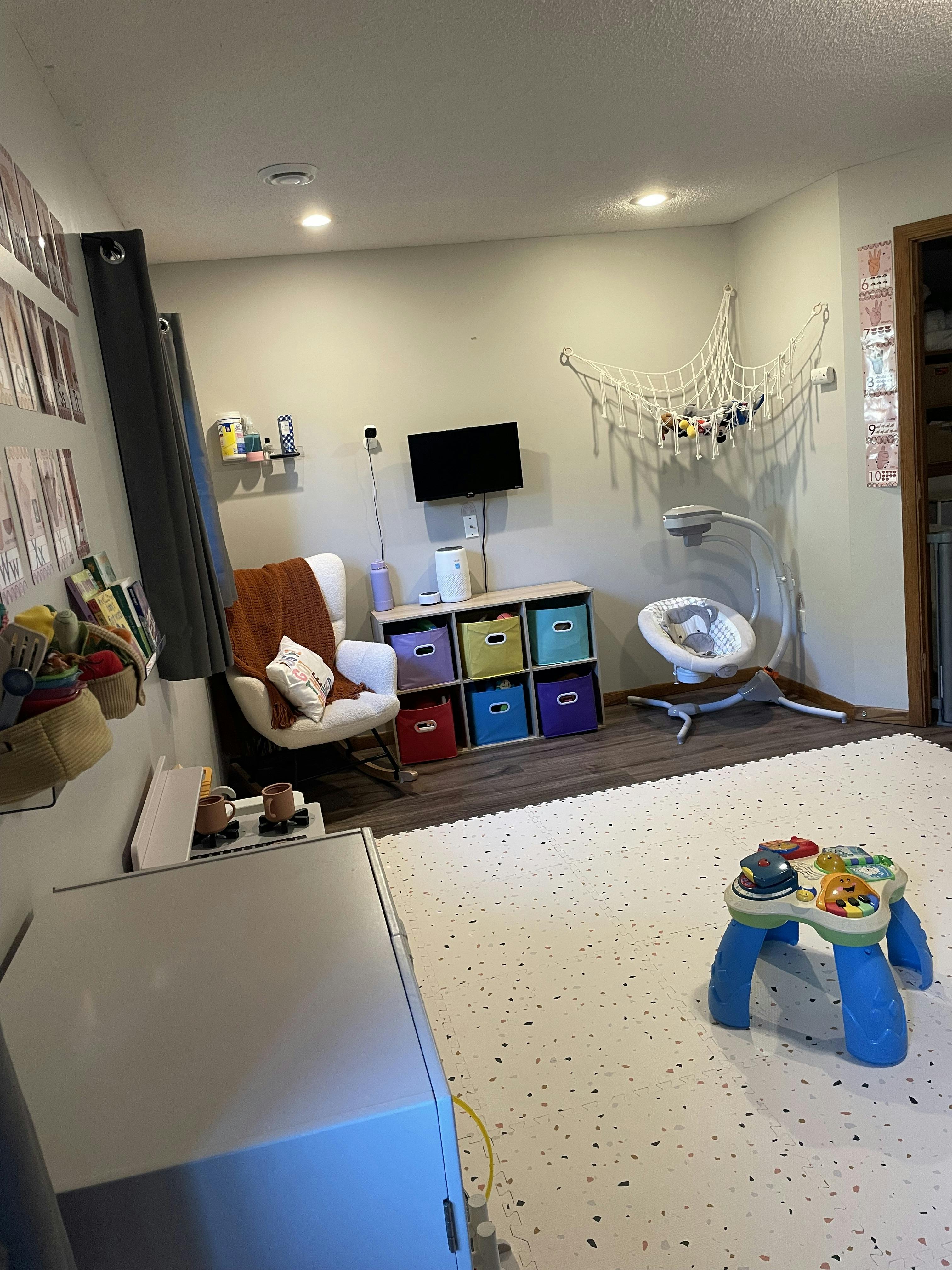 A room with a white rocking chair, a television, and a baby swing