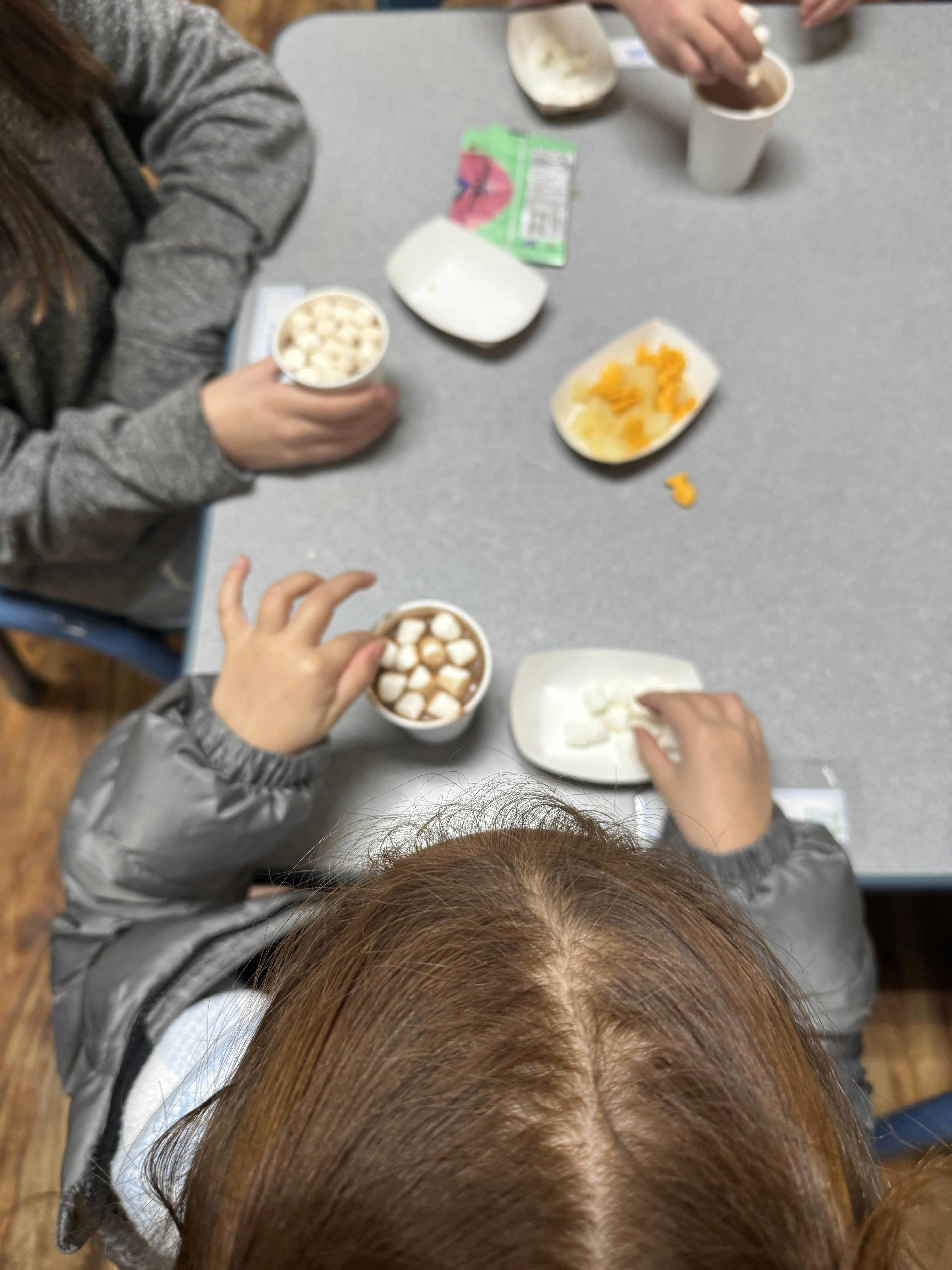 Two people adding marshmallows to cups of hot chocolate