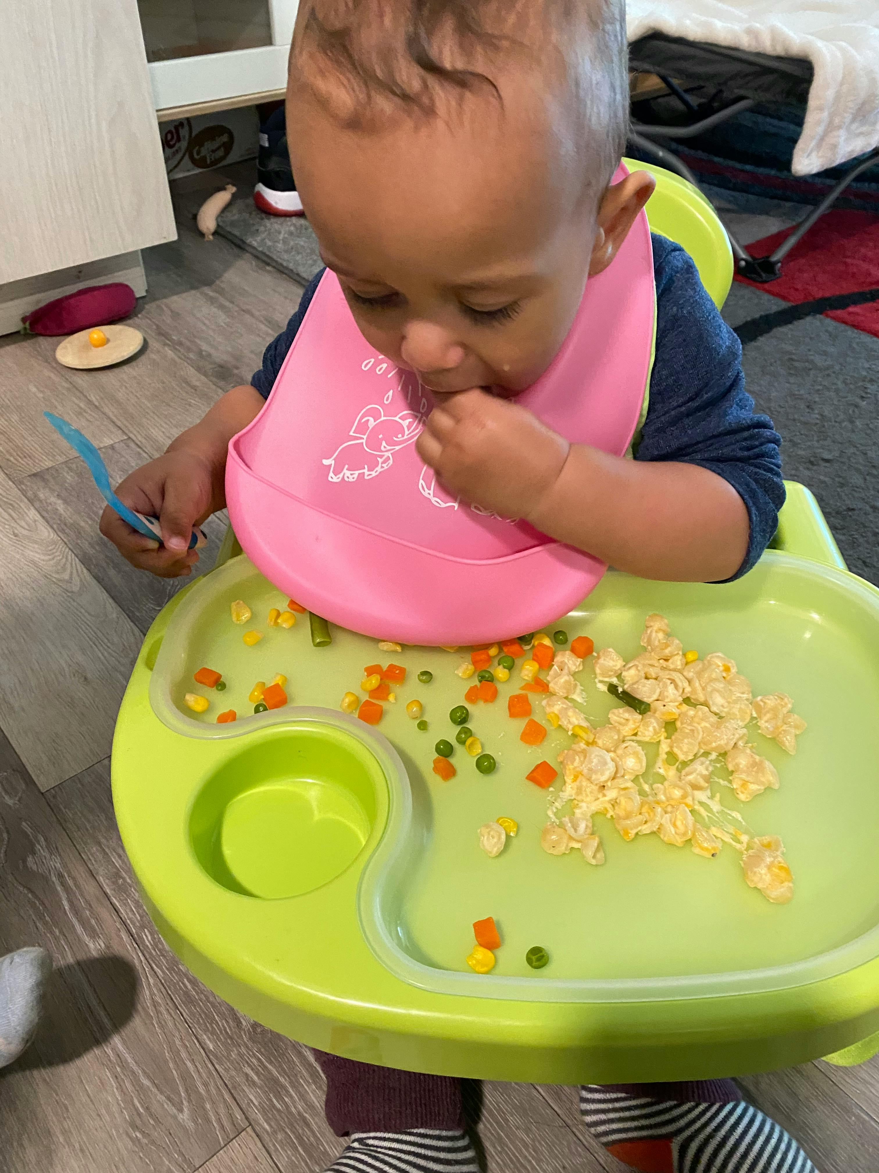 Child in a high chair with a pink bib eating food from the tray