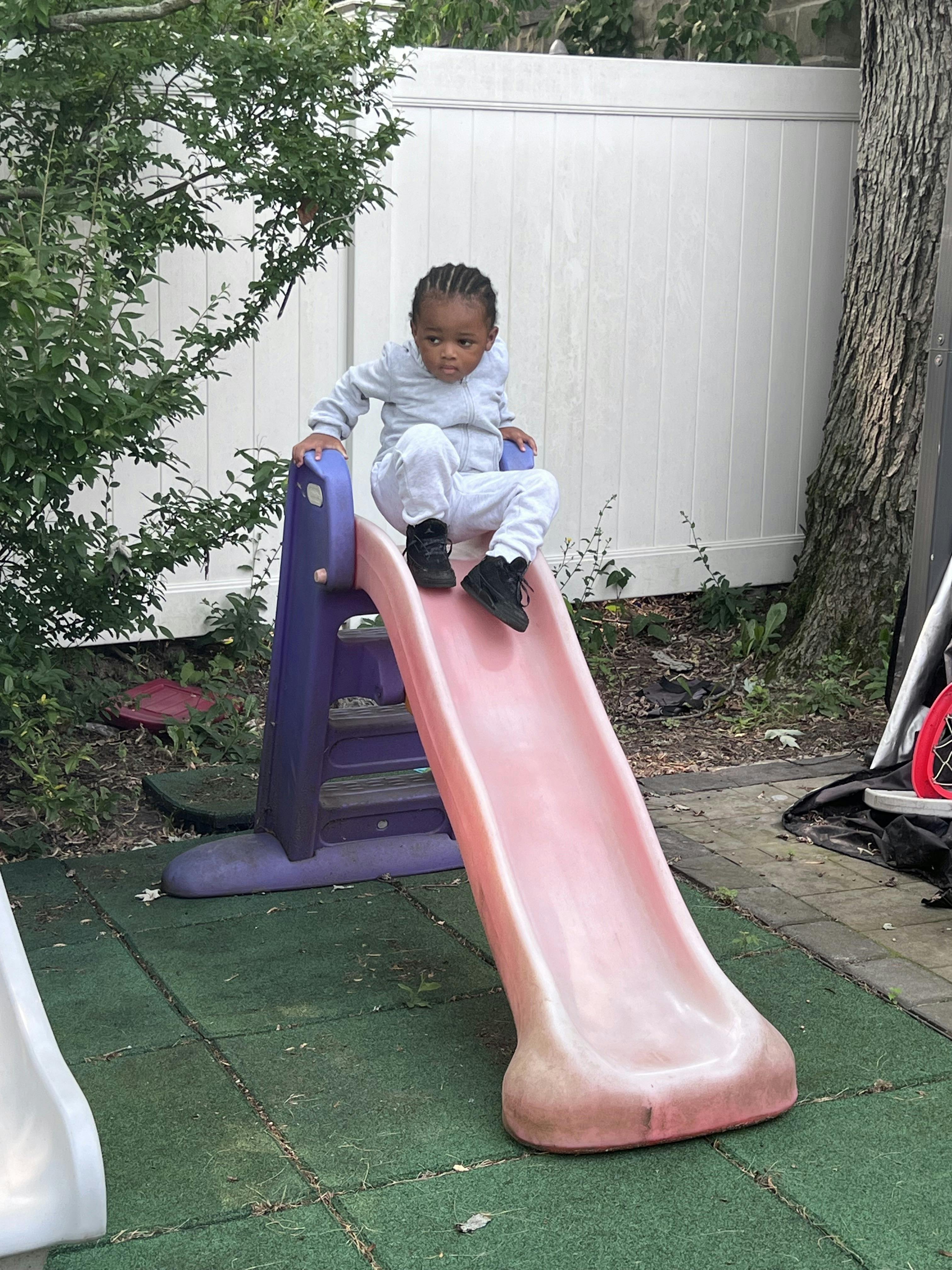 Child sitting at the top of a pink and purple slide