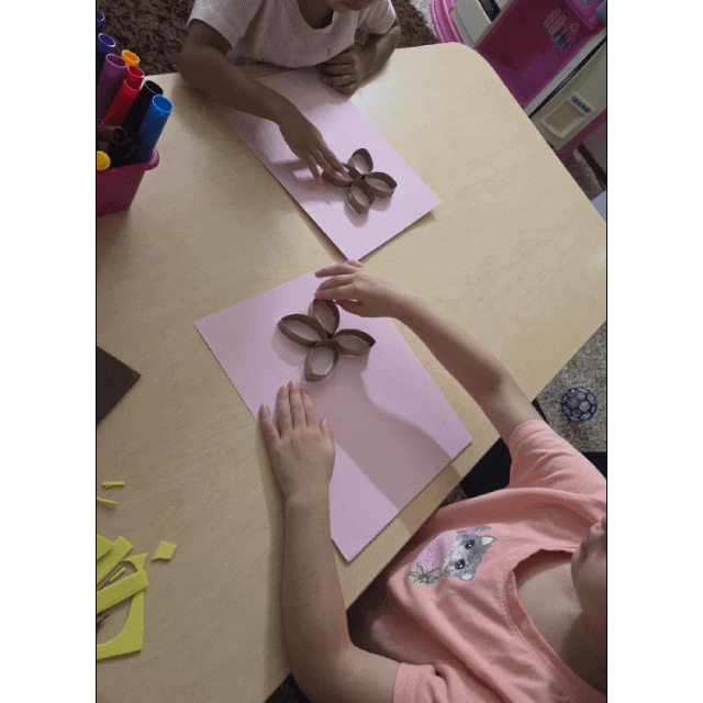Two people crafting flower shapes from cardboard tubes on pink paper