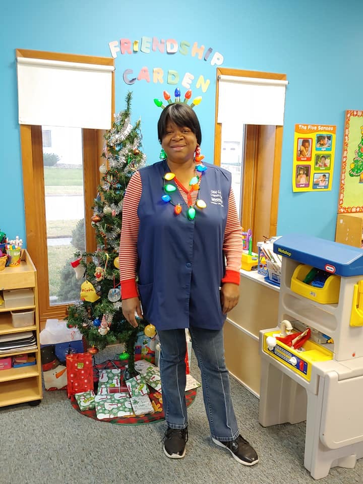Person wearing a light-up necklace standing next to a Christmas tree in a classroom