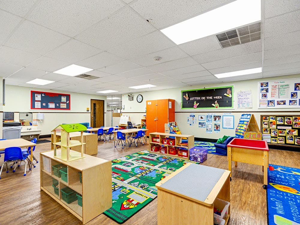Empty classroom with small tables, chairs, and play areas