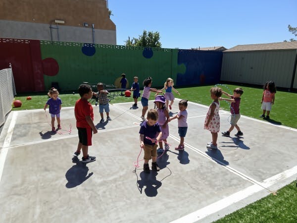 Group of children playing with jump ropes on an outdoor concrete court