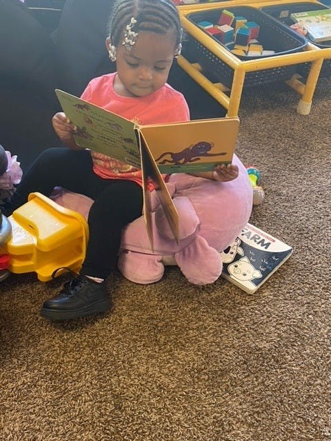 Child sitting on a plush toy and reading a book
