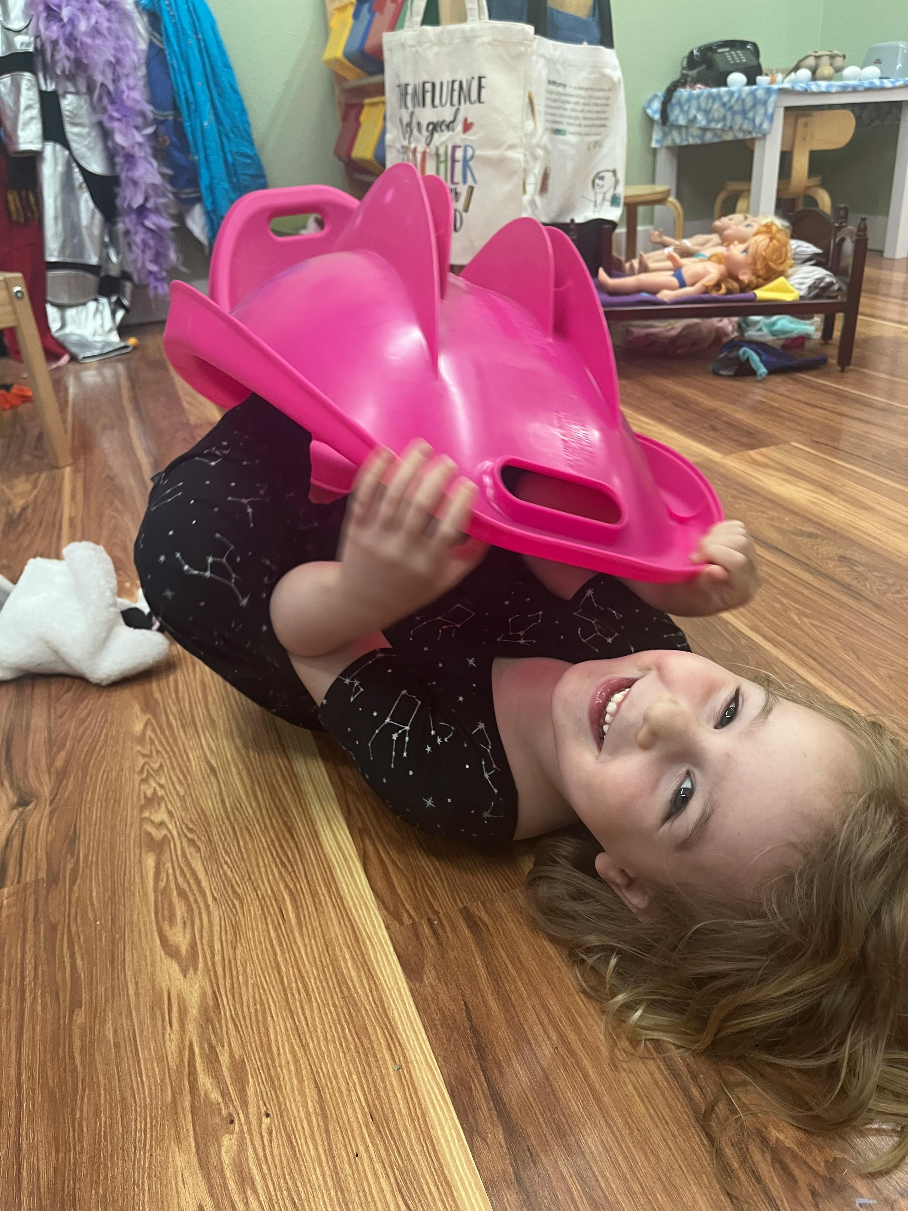 Child lying on floor holding a pink toy over their head