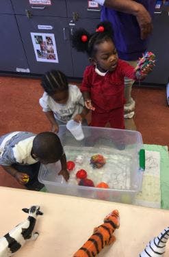 Three children playing with toys in a clear bin of water
