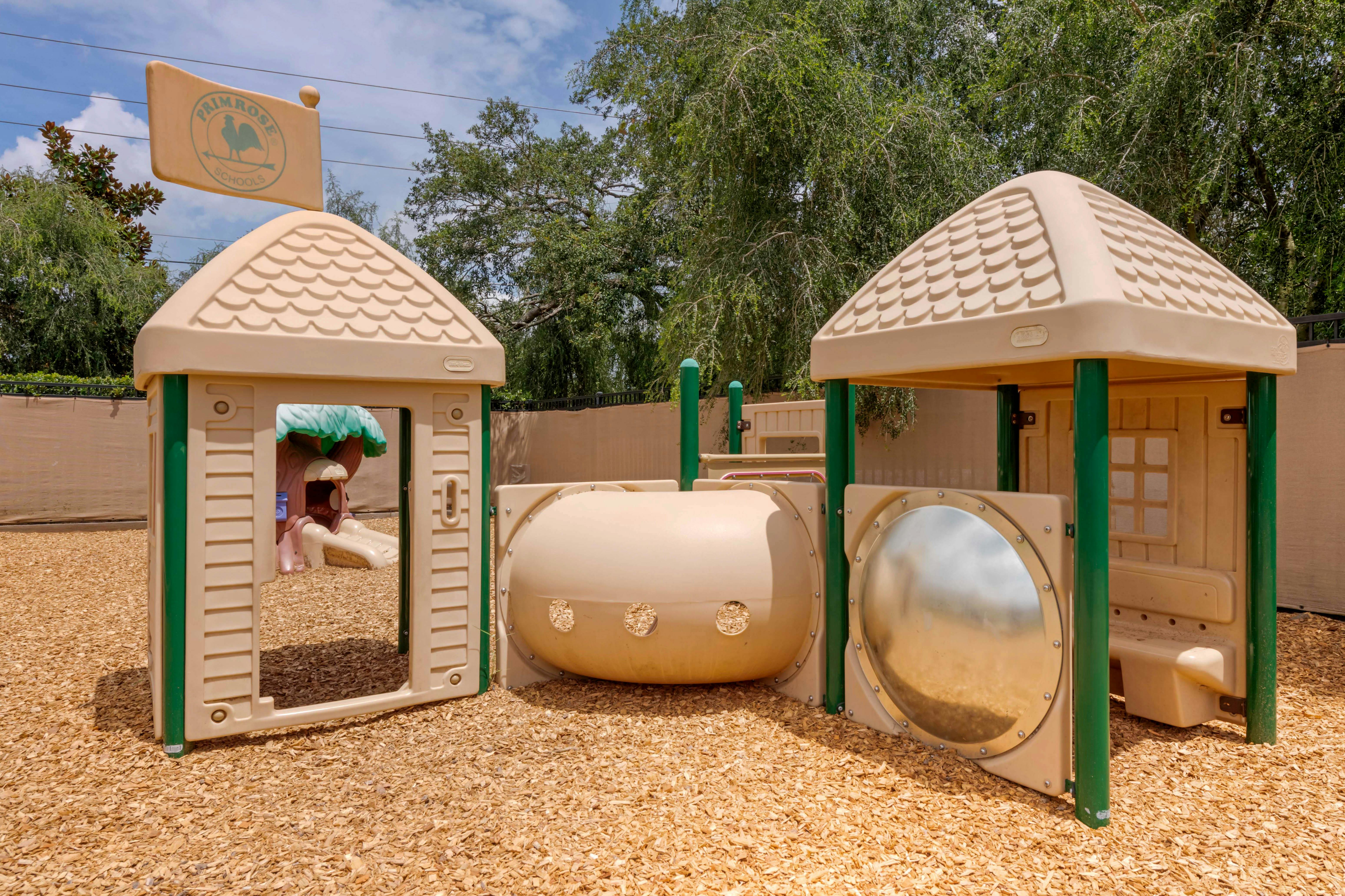 Playground equipment with a beige playhouse and tunnel on the left a sign that says Primrose Schools