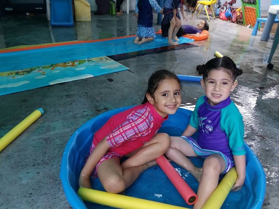 Two children sitting in a small blue pool with water