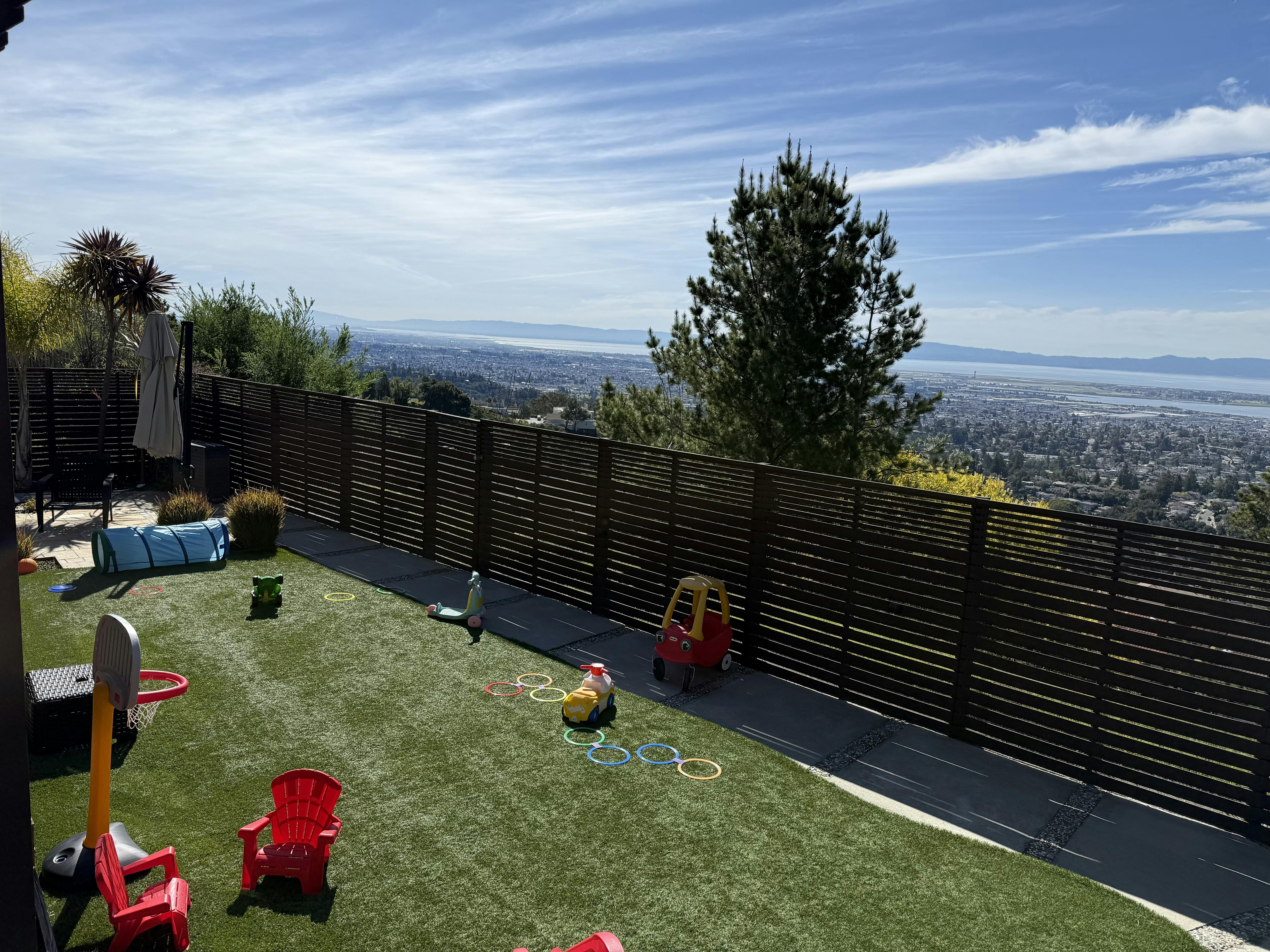 Backyard with artificial turf and toys overlooking a city and bay