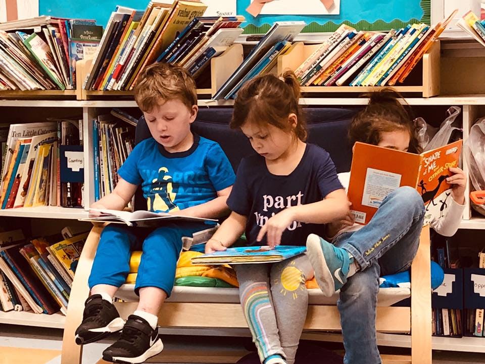 Three children reading books in a classroom