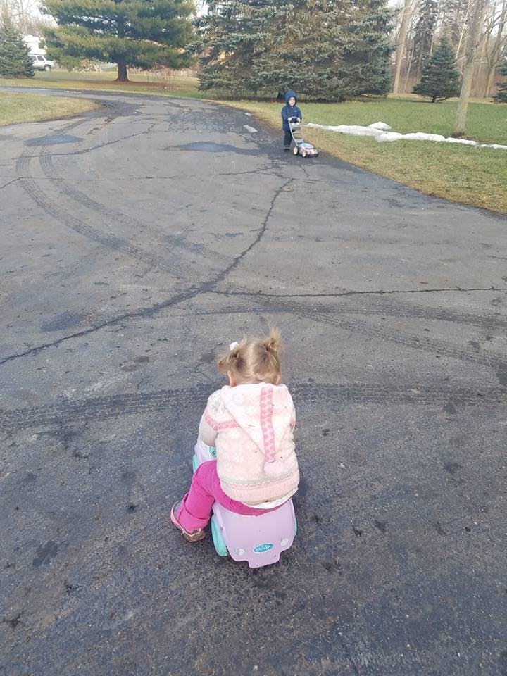 Child on a ride-on toy watching another child push a toy lawnmower