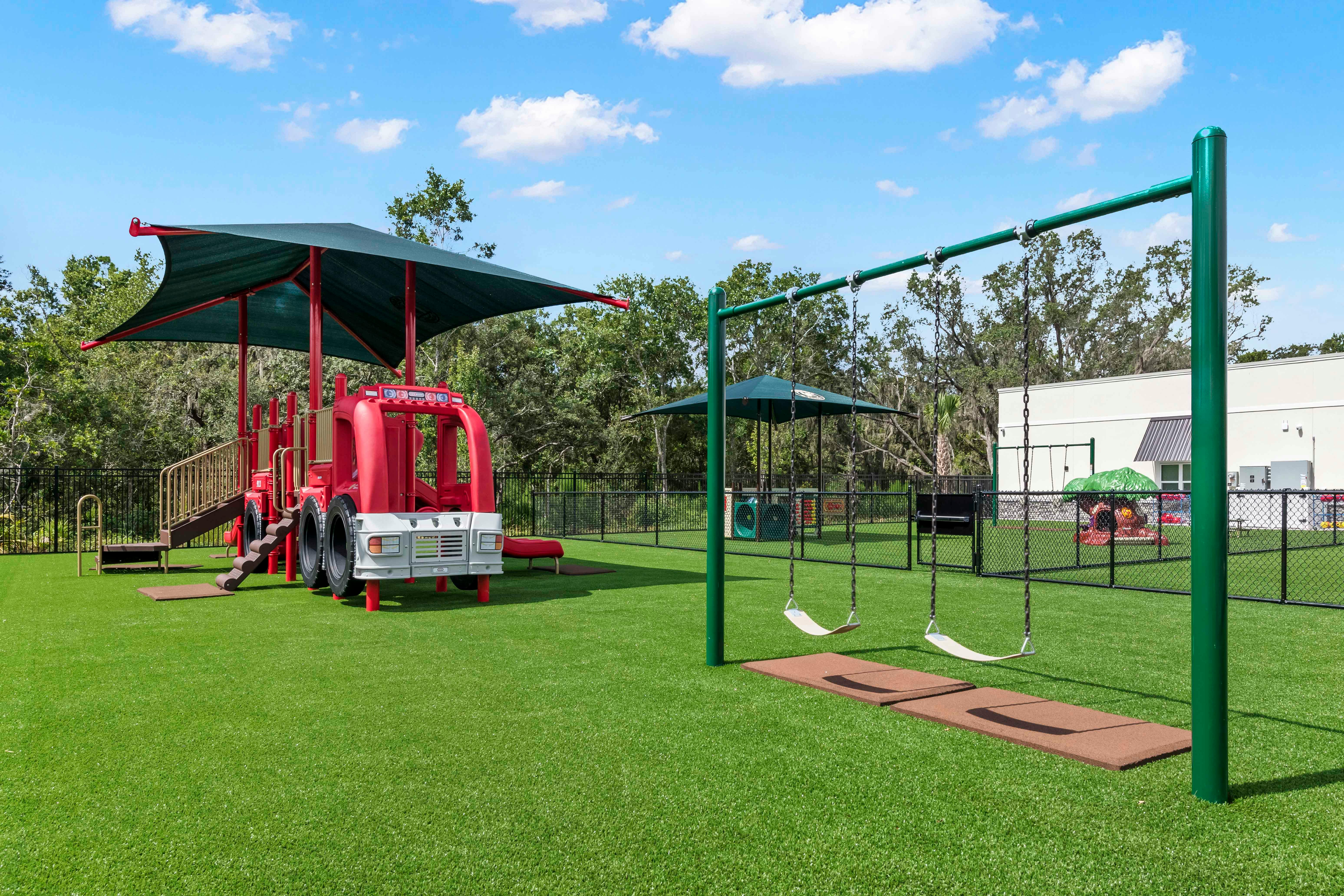 playground with a red fire truck structure and green swings