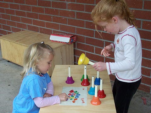 Two children playing with colorful handbells and a matching game