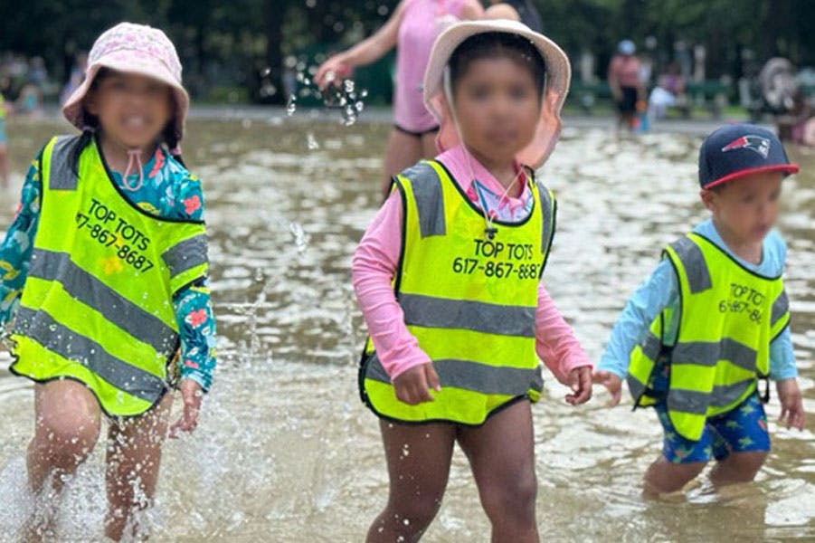 Three children in reflective vests wading in a shallow pool