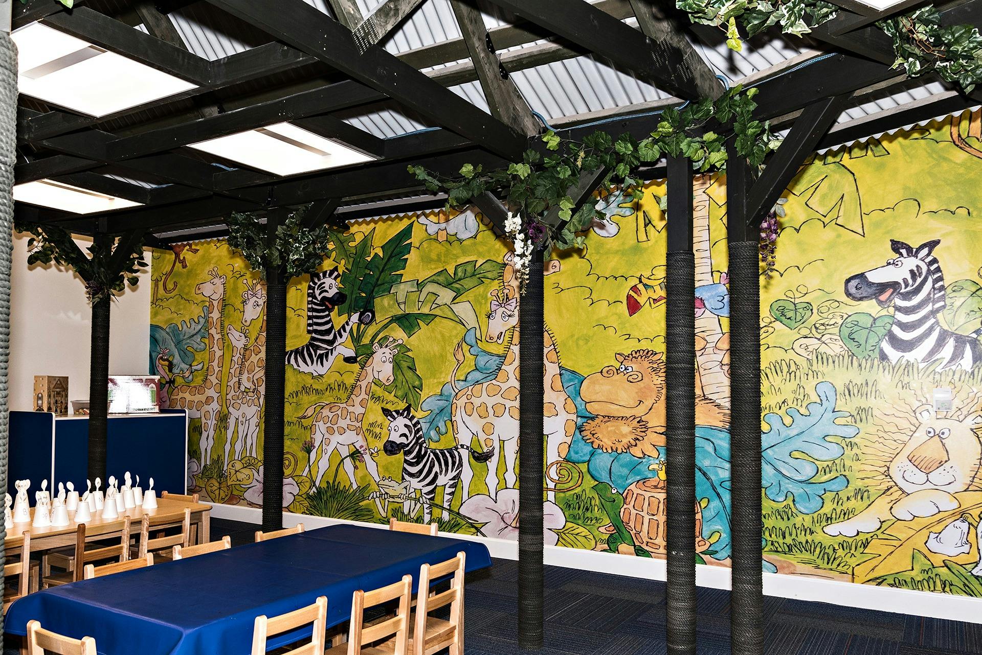 Room with tables and chairs, and a wall mural of cartoon animals