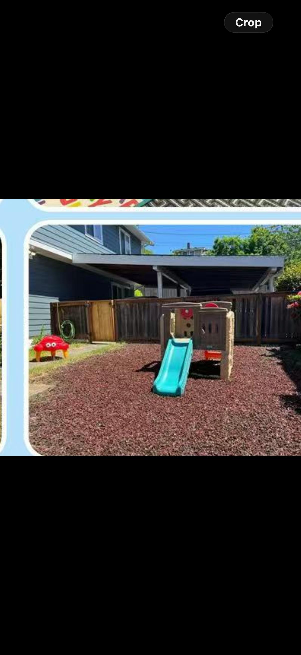backyard play area with a blue slide, red mulch, and wooden fence