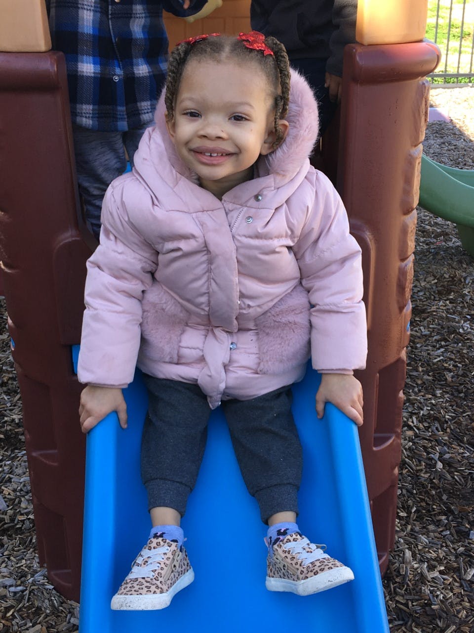 Child in a pink coat sitting on a blue slide