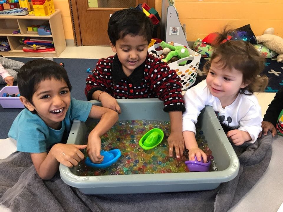 Three children playing with water beads in a bin