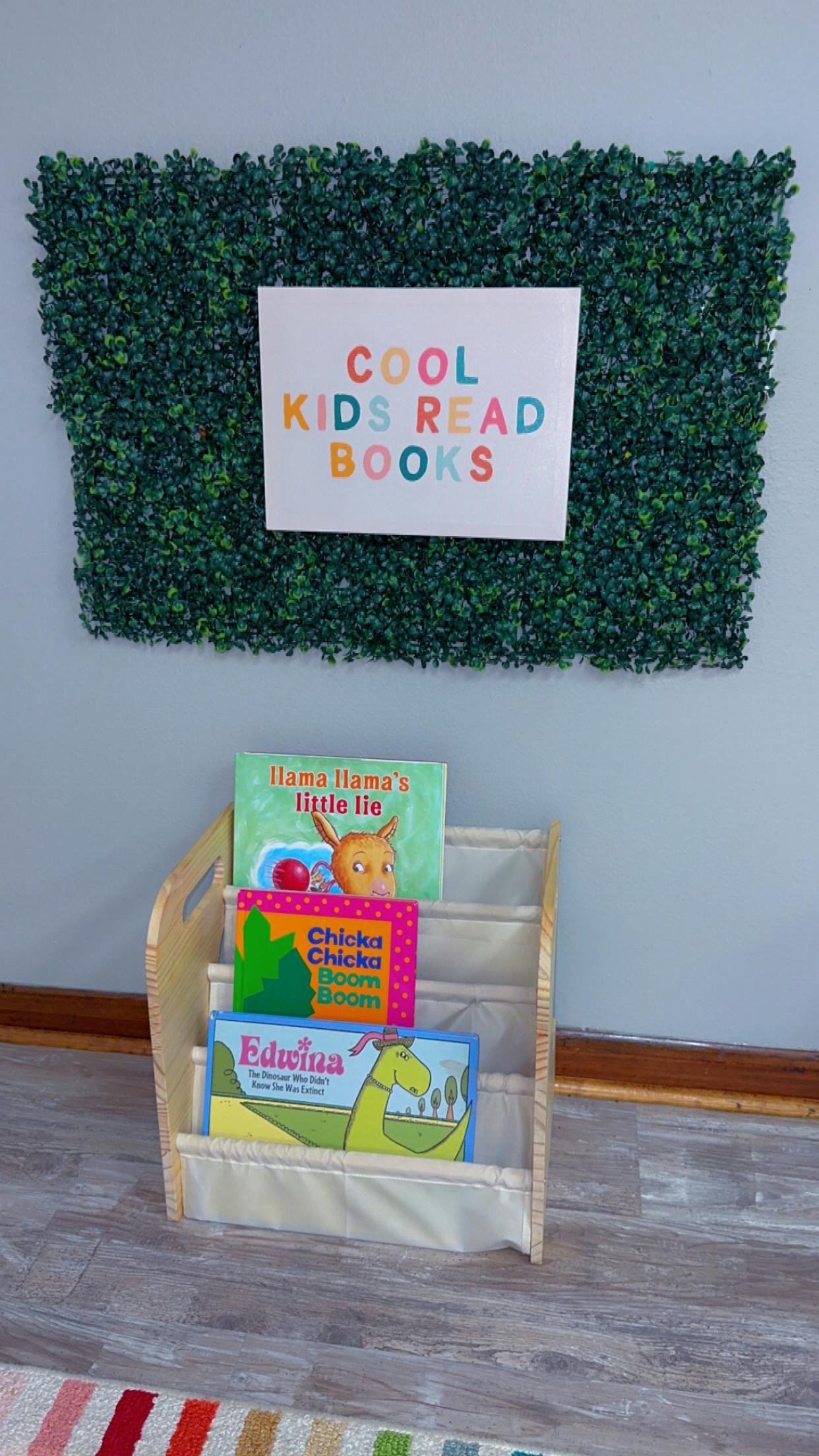 Sign on a green hedge wall that reads "Cool Kids Read Books" above a bookshelf