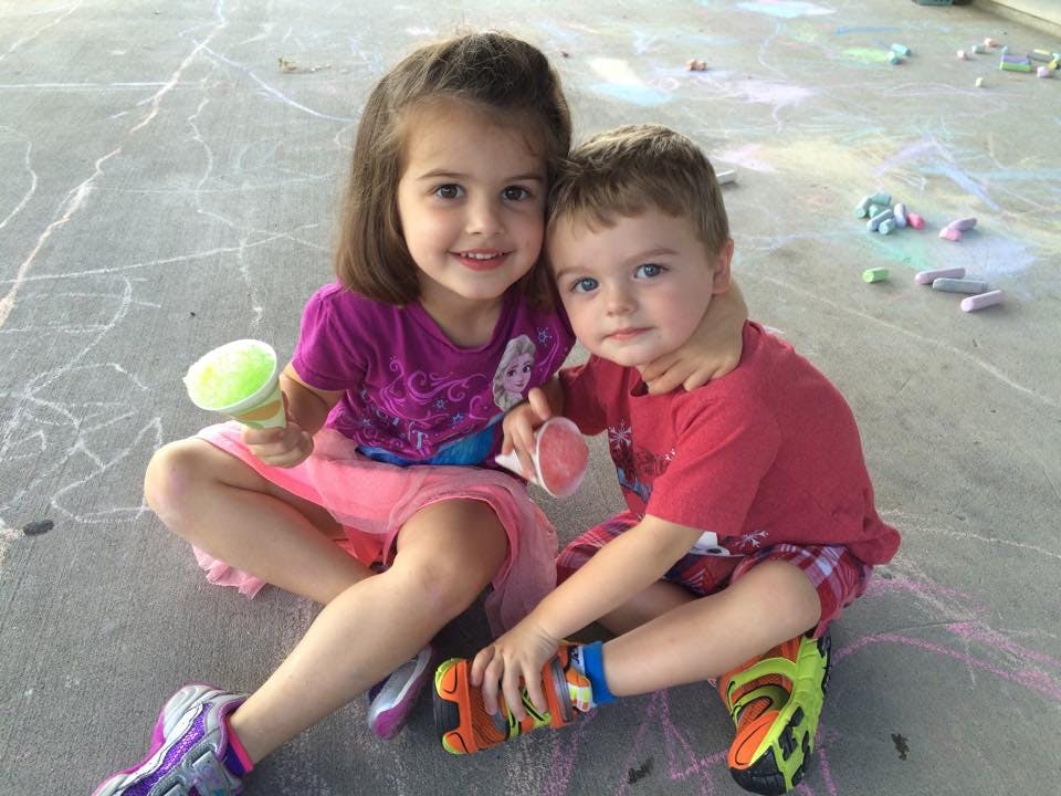 Two children sitting on the ground, one holding a cup