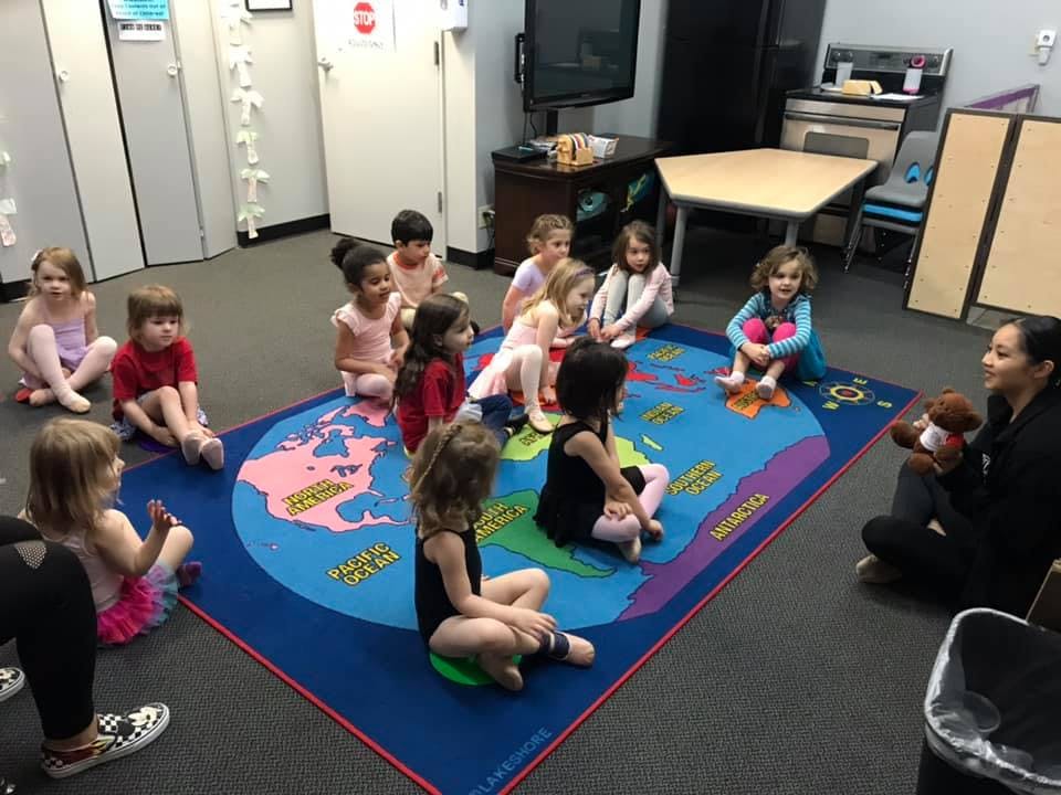 Children sitting on a world map rug listening to an adult