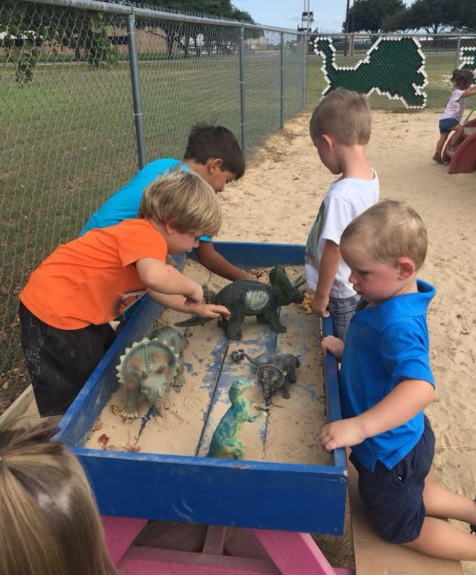 Children playing with dinosaur toys in a sandbox