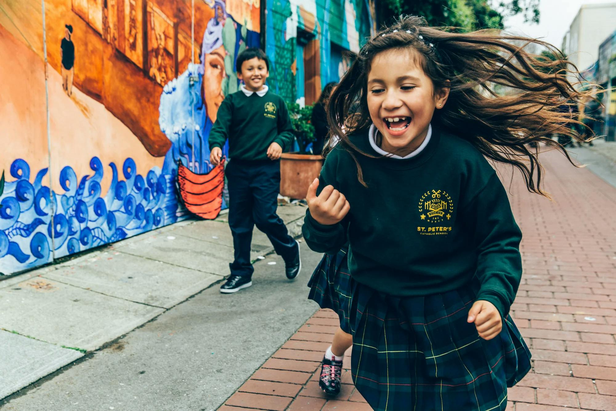 Child in uniform running with another child behind, hair flowing