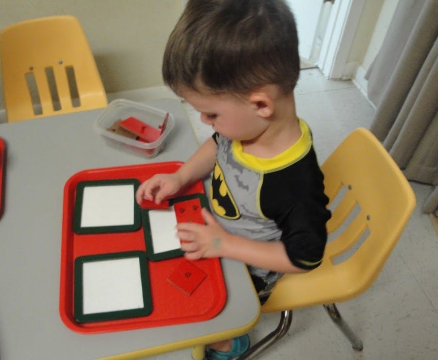Child playing with a puzzle on a red tray at a table