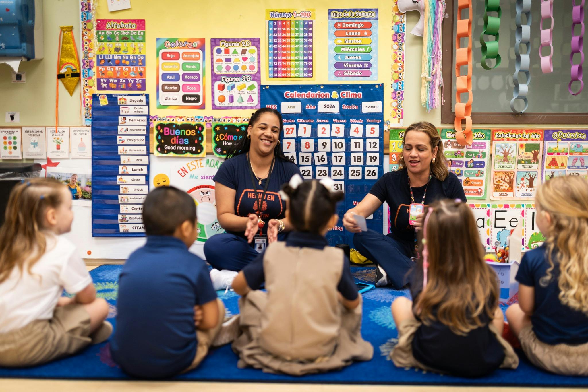 Two people teaching a group of children sitting on the floor in a classroom