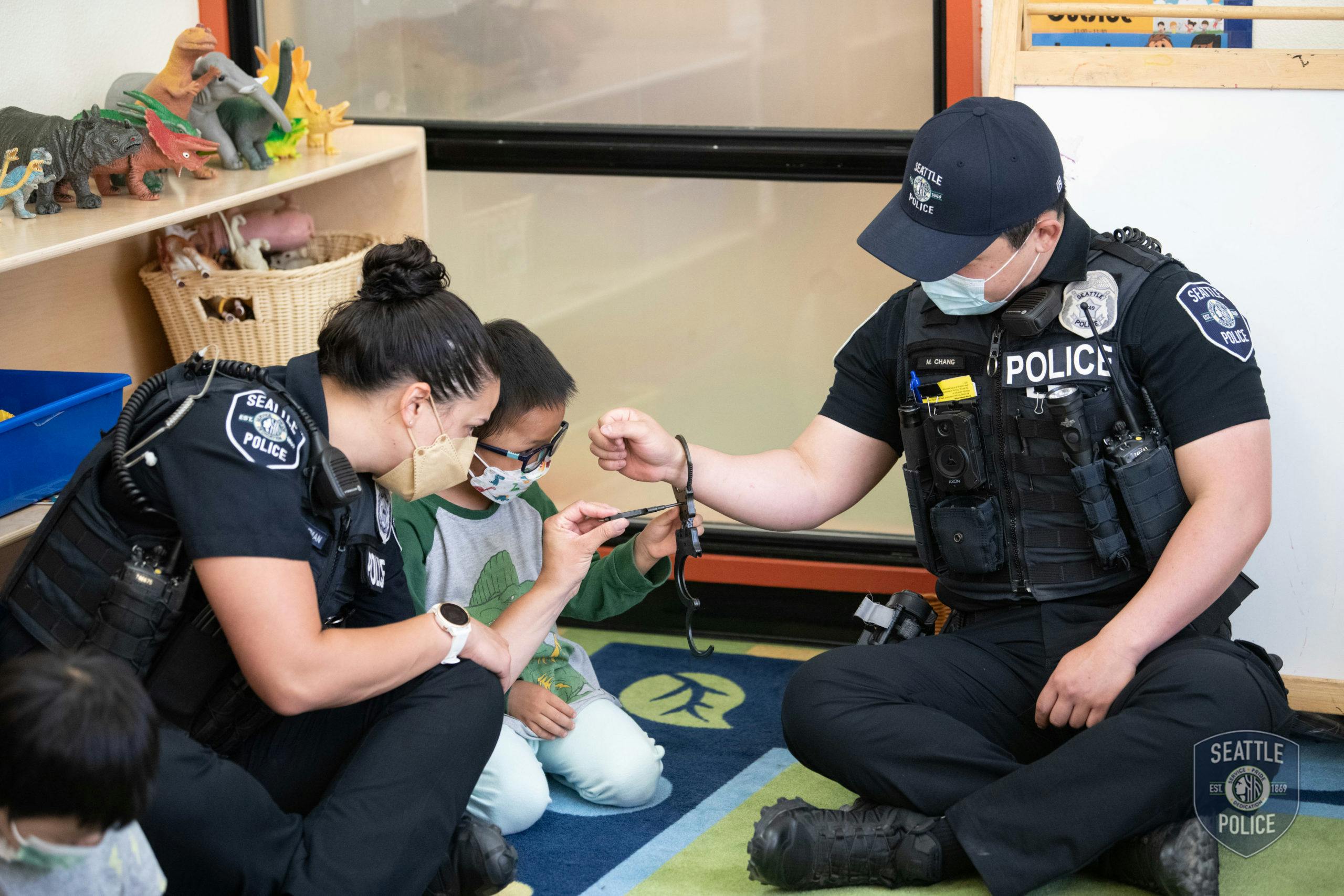Police officers and a child kneeling on a rug, holding handcuffs