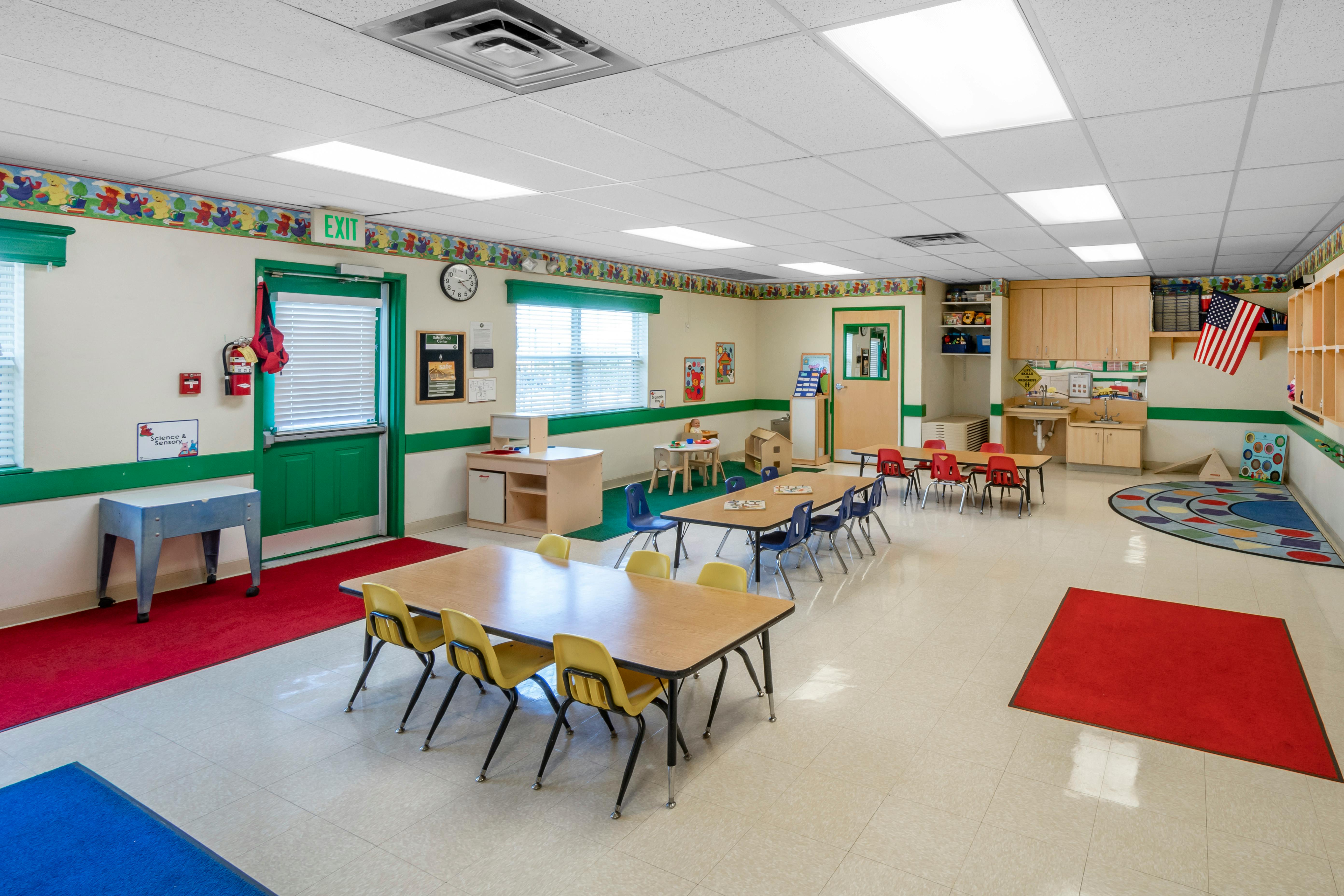 Colorful classroom with tables and chairs for children, an exit door, and a flag
