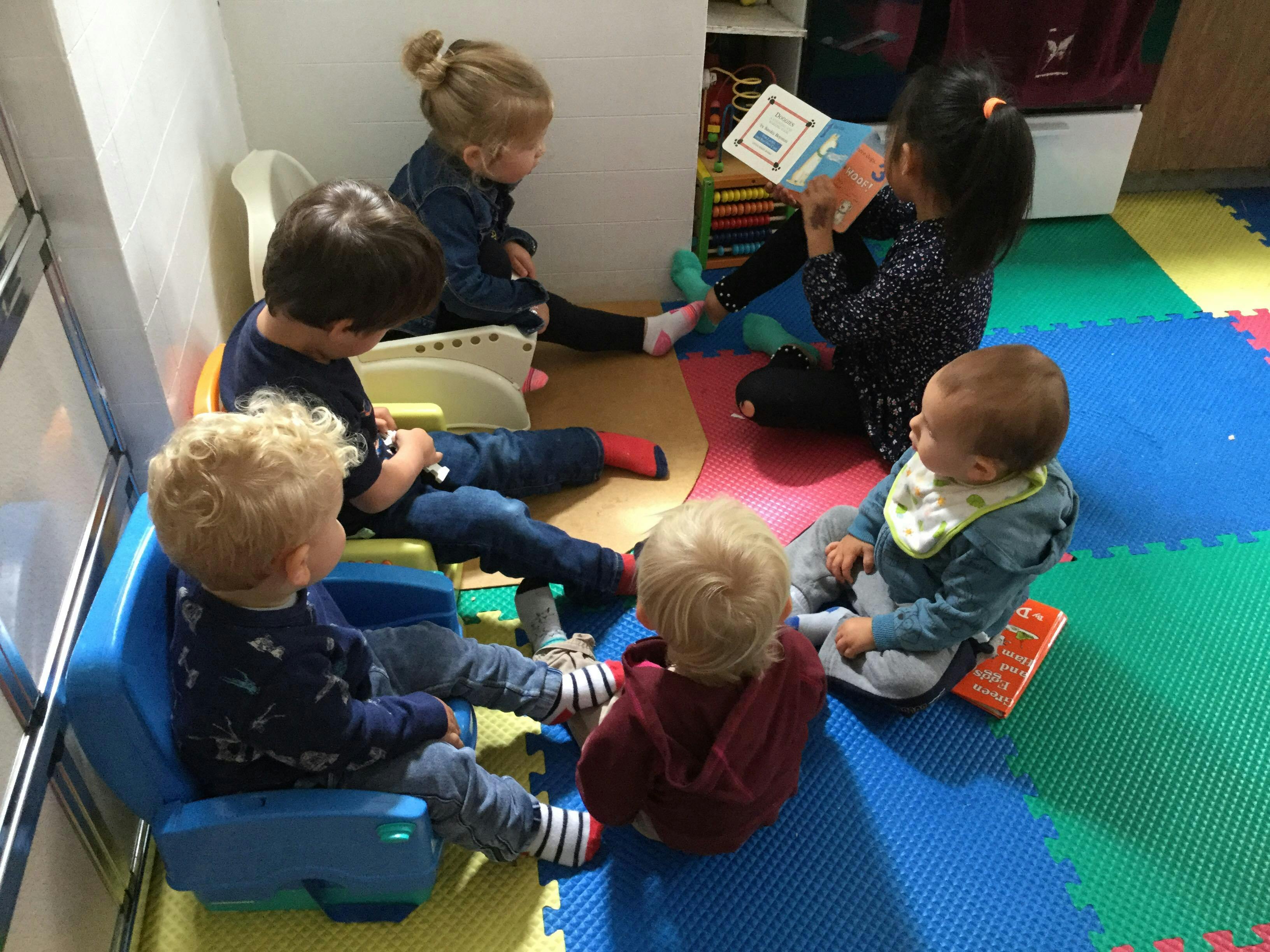 Children sitting on floor and chairs, one child reading a book