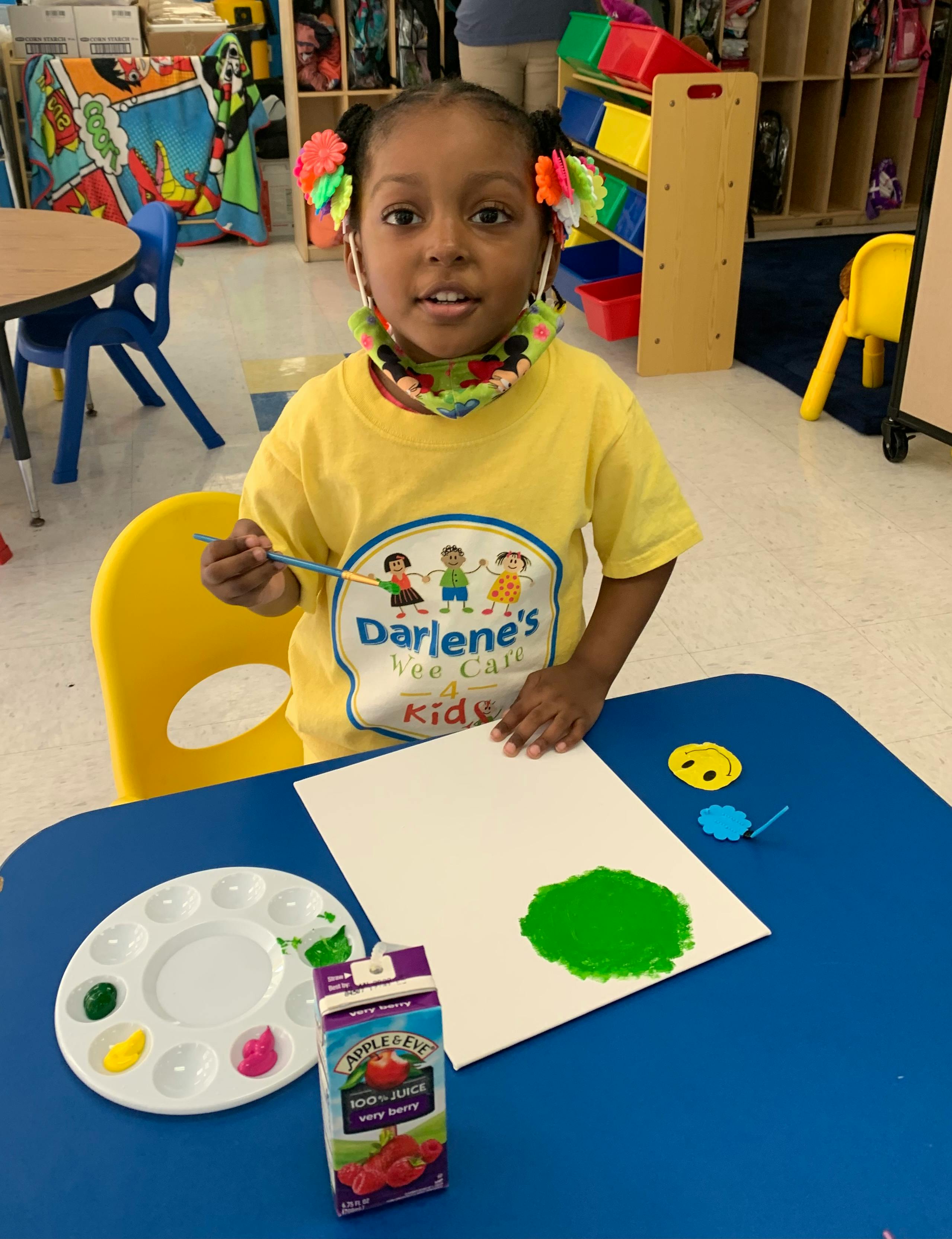 Child painting green on paper at a table
