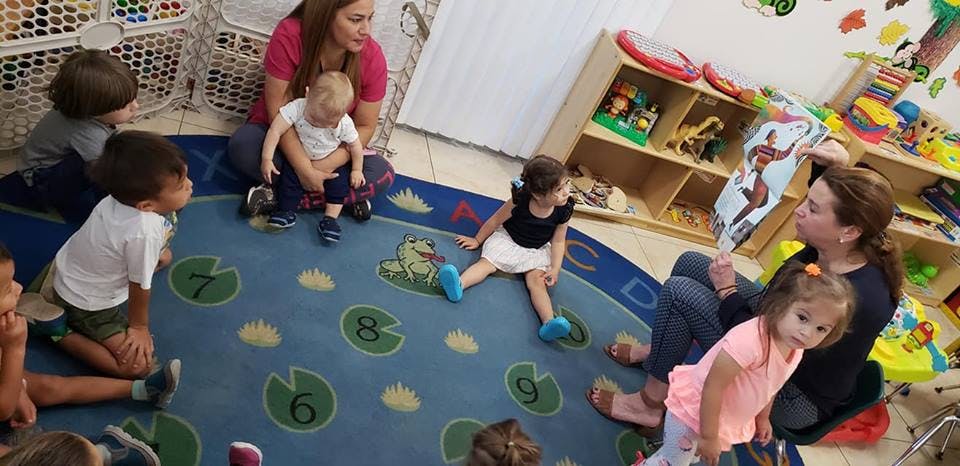 Adults and children sitting on a rug in a classroom
