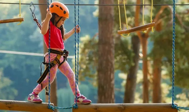 Child in harness and helmet walking on a rope bridge in an adventure park