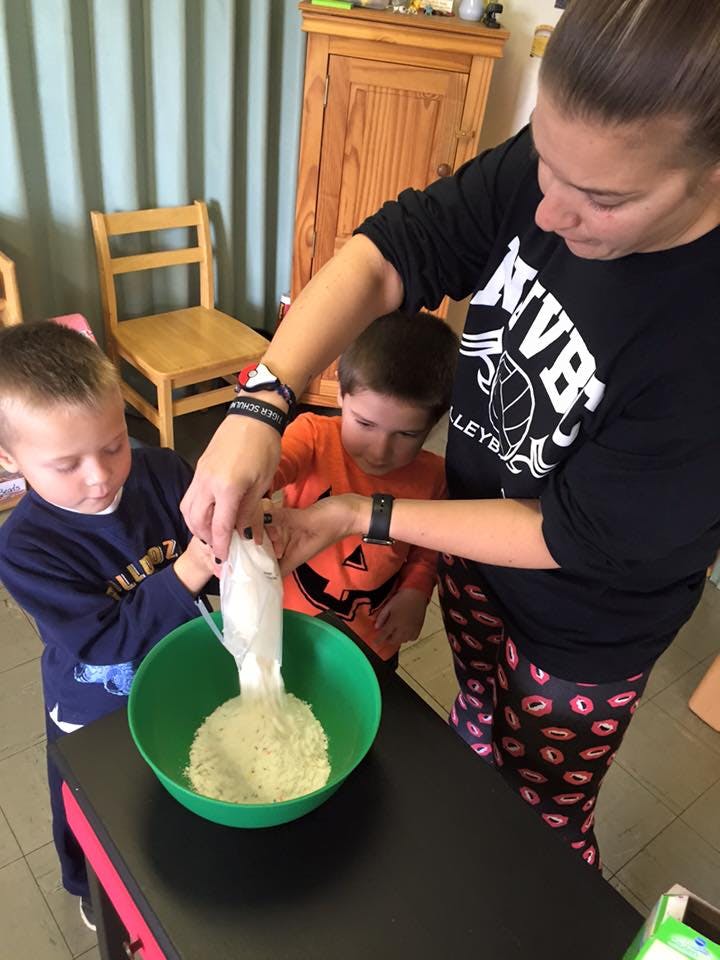 Person and two children pouring ingredients into a bowl