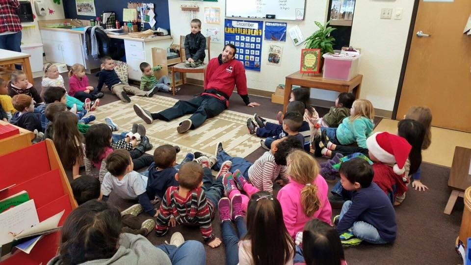 Adult sitting on floor with children gathered around in a classroom