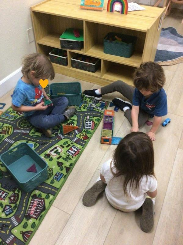 Three children playing with magnetic building blocks on a rug