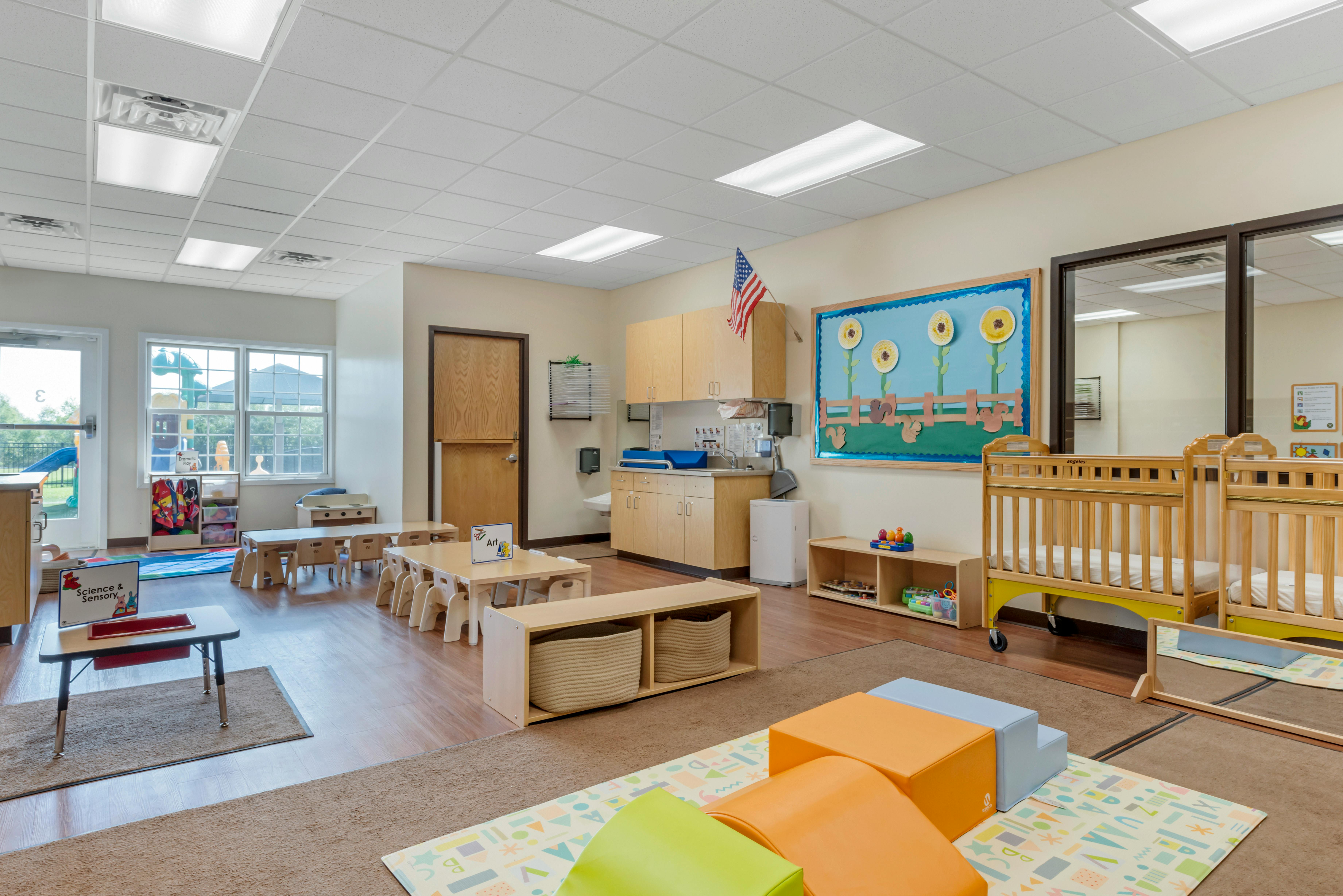 Classroom with cribs, small tables and chairs, and a play area