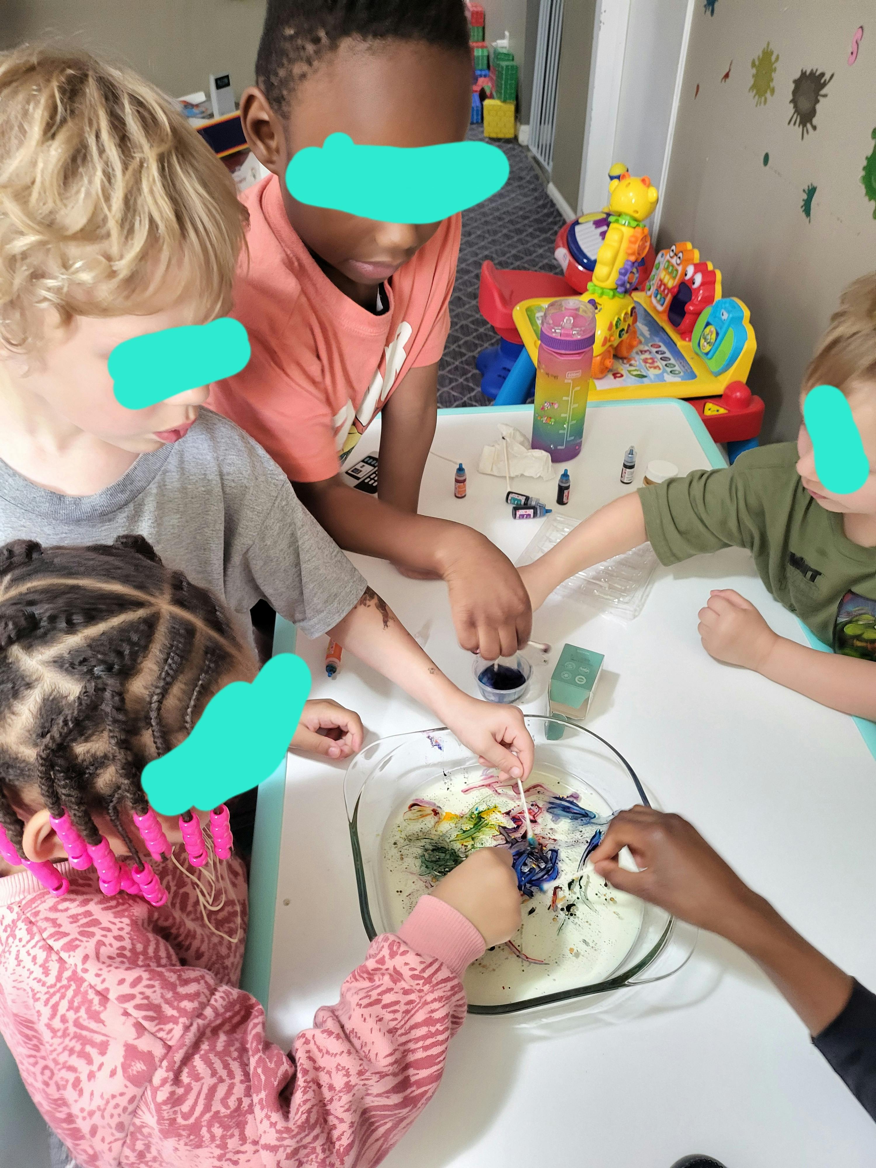 Four children doing a science experiment with colorful liquids in a glass dish