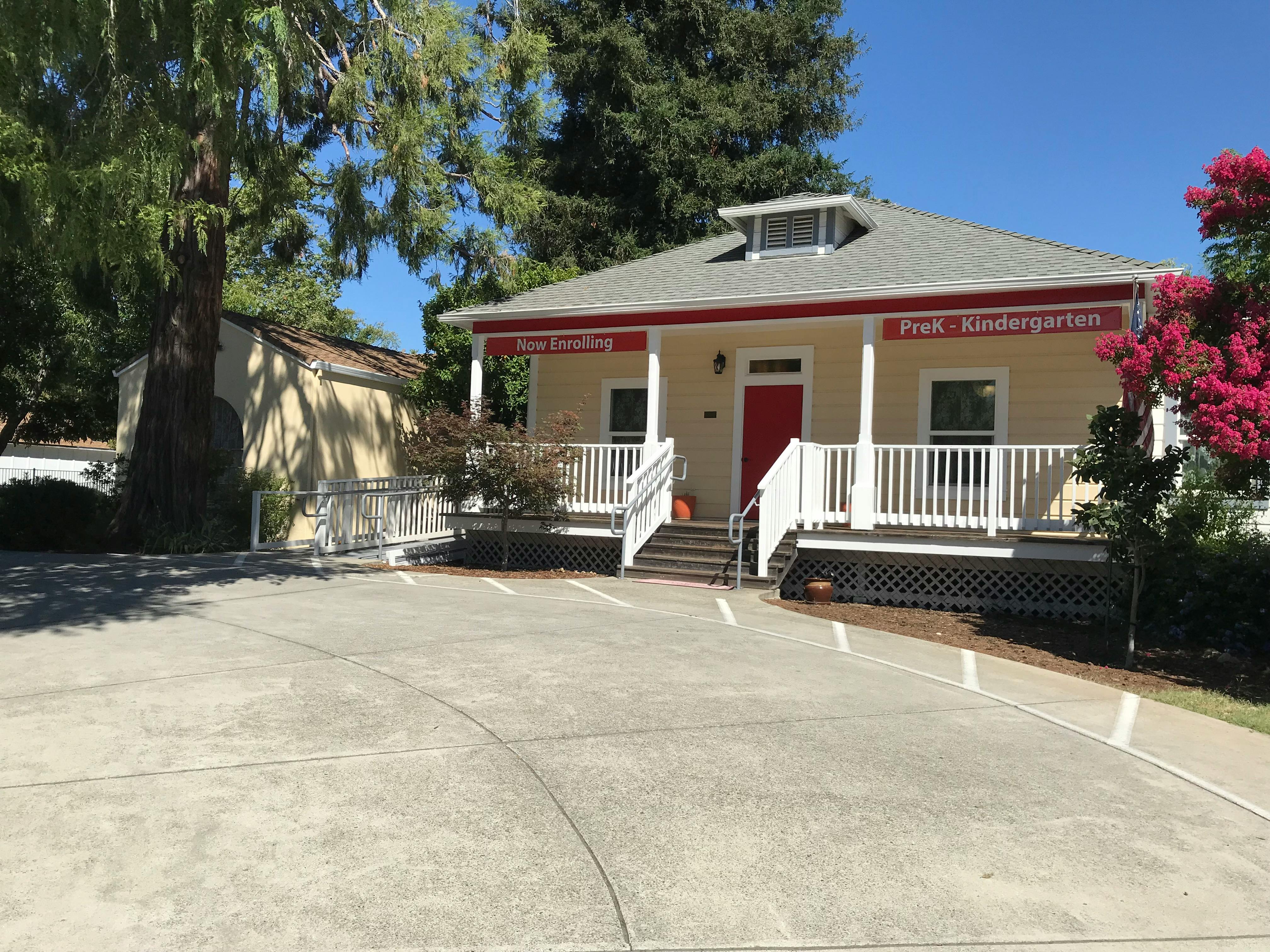 A cream-colored house with a red door and a porch with white railings
